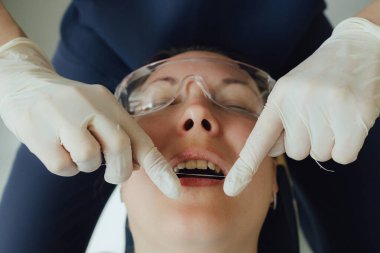 Genç bir dişçiye dişçi muayenesinde gülümseyen olgun bir kadın. Klinikte randevu. Diş beyazlatma, temizlik ya da oral, hastanede ağız ve sakız bakımı. Yumuşak odaklanma. Dizinin bir parçası. Yakın plan..