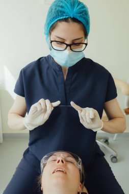 Genç bir dişçiye dişçi muayenesinde gülümseyen olgun bir kadın. Klinikte randevu. Diş beyazlatma, temizlik ya da oral, hastanede ağız ve sakız bakımı. Yumuşak odaklanma. Dizinin bir parçası. Yakın plan..