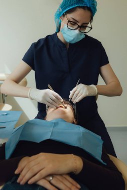 Genç bir dişçiye dişçi muayenesinde gülümseyen olgun bir kadın. Klinikte randevu. Diş beyazlatma, temizlik ya da oral, hastanede ağız ve sakız bakımı. Yumuşak odaklanma. Dizinin bir parçası. Yakın plan..