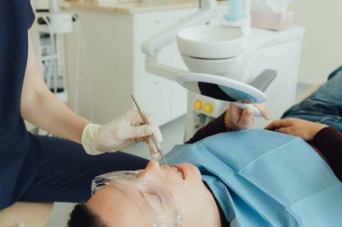 Genç bir dişçiye dişçi muayenesinde gülümseyen olgun bir kadın. Klinikte randevu. Diş beyazlatma, temizlik ya da oral, hastanede ağız ve sakız bakımı. Yumuşak odaklanma. Dizinin bir parçası. Yakın plan..