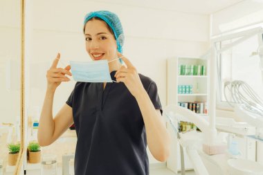 Randevuya hazırlanan genç dişçi maske takıyor. Tıpta kadın, diş bakımı, klinikte check-up. Diş beyazlatma, temizlik ya da oral, ağız ve sakız bakımı. Bir serinin parçası.