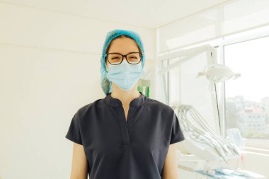 Randevuya hazırlanan genç dişçi maske takıyor. Tıpta kadın, diş bakımı, klinikte check-up. Diş beyazlatma, temizlik ya da oral, ağız ve sakız bakımı. Bir serinin parçası.