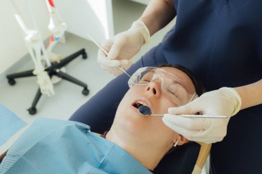 Genç bir dişçiye dişçi muayenesinde gülümseyen olgun bir kadın. Klinikte randevu. Diş beyazlatma, temizlik ya da oral, hastanede ağız ve sakız bakımı. Yumuşak odaklanma. Dizinin bir parçası. Yakın plan..