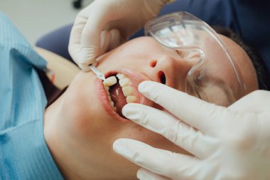 Genç bir dişçiye dişçi muayenesinde gülümseyen olgun bir kadın. Klinikte randevu. Diş beyazlatma, temizlik ya da oral, hastanede ağız ve sakız bakımı. Yumuşak odaklanma. Dizinin bir parçası. Yakın plan..