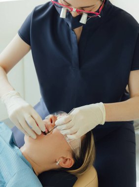 Genç bir dişçiye dişçi muayenesinde gülümseyen olgun bir kadın. Klinikte randevu. Diş beyazlatma, temizlik ya da oral, hastanede ağız ve sakız bakımı. Yumuşak odaklanma. Dizinin bir parçası. Yakın plan..