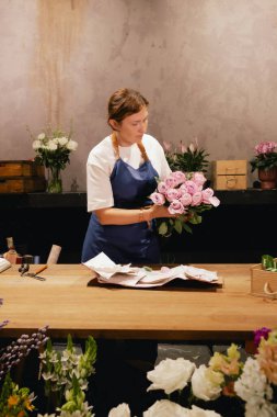 Önlüklü orta yaşlı kadın çiçekçi çiçekçide çiçek buketi için çiçek düzenliyor. Küçük bir yerel işletme. Dizinin bir parçası. Yumuşak odak