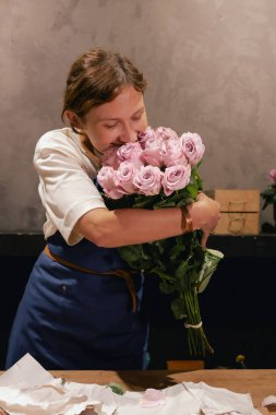 Önlüklü orta yaşlı kadın çiçekçi çiçekçide çiçek buketi için çiçek düzenliyor. Küçük bir yerel işletme. Dizinin bir parçası. Yumuşak odak