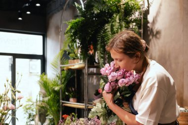 Önlüklü orta yaşlı kadın çiçekçi çiçekçide çiçek buketi için çiçek düzenliyor. Küçük bir yerel işletme. Dizinin bir parçası. Yumuşak odak
