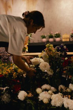Önlüklü orta yaşlı kadın çiçekçi çiçekçide çiçek buketi için çiçek düzenliyor. Küçük bir yerel işletme. Dizinin bir parçası. Yumuşak odak