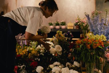 Önlüklü orta yaşlı kadın çiçekçi çiçekçide çiçek buketi için çiçek düzenliyor. Küçük bir yerel işletme. Dizinin bir parçası. Yumuşak odak