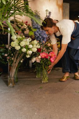 Önlüklü orta yaşlı kadın çiçekçi çiçekçide çiçek buketi için çiçek düzenliyor. Küçük bir yerel işletme. Dizinin bir parçası. Yumuşak odak