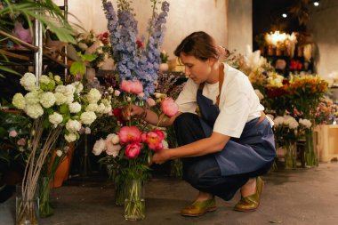 Önlüklü orta yaşlı kadın çiçekçi çiçekçide çiçek buketi için çiçek düzenliyor. Küçük bir yerel işletme. Dizinin bir parçası. Yumuşak odak