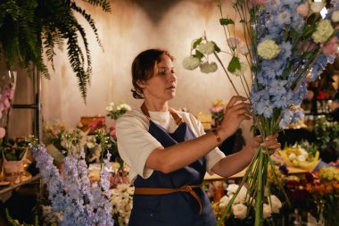 Önlüklü orta yaşlı kadın çiçekçi çiçekçide çiçek buketi için çiçek düzenliyor. Küçük bir yerel işletme. Dizinin bir parçası. Yumuşak odak