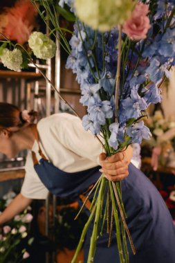 Önlüklü orta yaşlı kadın çiçekçi çiçekçide çiçek buketi için çiçek düzenliyor. Küçük bir yerel işletme. Dizinin bir parçası. Yumuşak odak