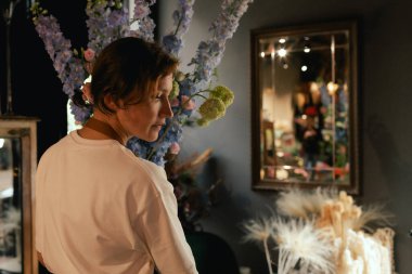 Önlüklü orta yaşlı kadın çiçekçi çiçekçide çiçek buketi için çiçek düzenliyor. Küçük bir yerel işletme. Dizinin bir parçası. Yumuşak odak