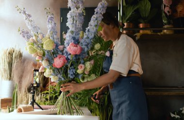 Önlüklü orta yaşlı kadın çiçekçi çiçekçide çiçek buketi için çiçek düzenliyor. Küçük bir yerel işletme. Dizinin bir parçası. Yumuşak odak