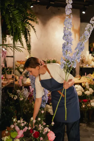 Önlüklü orta yaşlı kadın çiçekçi çiçekçide çiçek buketi için çiçek düzenliyor. Küçük bir yerel işletme. Dizinin bir parçası. Yumuşak odak