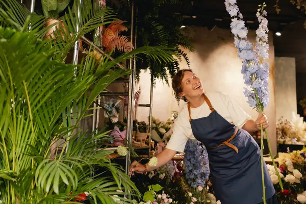 Önlüklü orta yaşlı kadın çiçekçi çiçekçide çiçek buketi için çiçek düzenliyor. Küçük bir yerel işletme. Dizinin bir parçası. Yumuşak odak