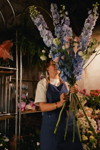 Önlüklü orta yaşlı kadın çiçekçi çiçekçide çiçek buketi için çiçek düzenliyor. Küçük bir yerel işletme. Dizinin bir parçası. Yumuşak odak
