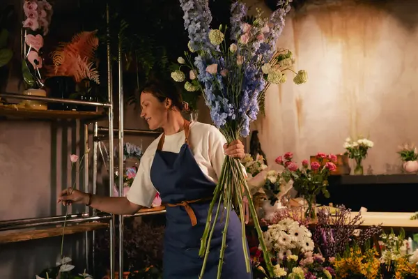 Önlüklü orta yaşlı kadın çiçekçi çiçekçide çiçek buketi için çiçek düzenliyor. Küçük bir yerel işletme. Dizinin bir parçası. Yumuşak odak