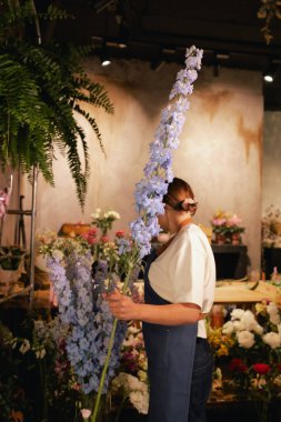 Önlüklü orta yaşlı kadın çiçekçi çiçekçide çiçek buketi için çiçek düzenliyor. Küçük bir yerel işletme. Dizinin bir parçası. Yumuşak odak