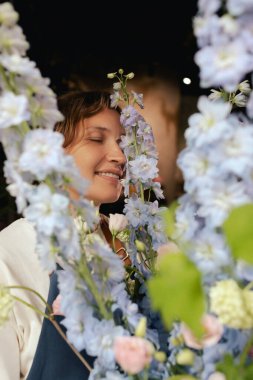 Önlüklü orta yaşlı kadın çiçekçi çiçekçide çiçek buketi için çiçek düzenliyor. Küçük bir yerel işletme. Dizinin bir parçası. Yumuşak odak