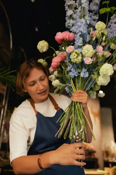 Önlüklü orta yaşlı kadın çiçekçi çiçekçide çiçek buketi için çiçek düzenliyor. Küçük bir yerel işletme. Dizinin bir parçası. Yumuşak odak