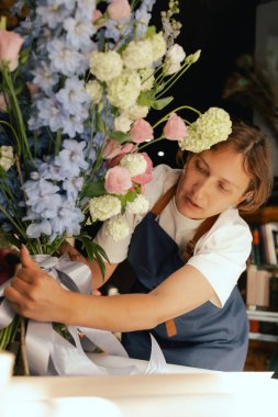 Önlüklü orta yaşlı kadın çiçekçi çiçek buketi için taze çiçek ayarlıyor çiçekçinin buketine bir kurdele bağlıyor. Küçük bir yerel işletme. Dizinin bir parçası. Yumuşak odak.
