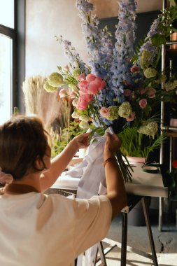 Önlüklü orta yaşlı kadın çiçekçi çiçek buketi için taze çiçek ayarlıyor çiçekçinin buketine bir kurdele bağlıyor. Küçük bir yerel işletme. Dizinin bir parçası. Yumuşak odak.