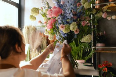 Önlüklü orta yaşlı kadın çiçekçi çiçek buketi için taze çiçek ayarlıyor çiçekçinin buketine bir kurdele bağlıyor. Küçük bir yerel işletme. Dizinin bir parçası. Yumuşak odak.