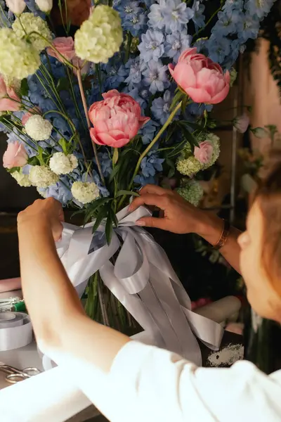 Önlüklü orta yaşlı kadın çiçekçi çiçek buketi için taze çiçek ayarlıyor çiçekçinin buketine bir kurdele bağlıyor. Küçük bir yerel işletme. Dizinin bir parçası. Yumuşak odak.