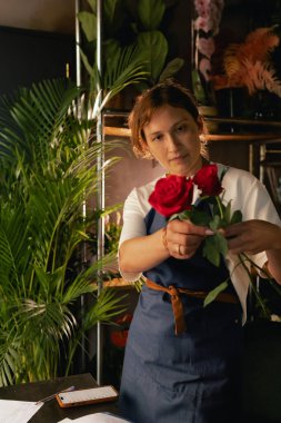 Önlüklü orta yaşlı kadın çiçekçi çiçekçide çiçek buketi için çiçek düzenliyor. Küçük bir yerel işletme. Dizinin bir parçası. Yumuşak odak