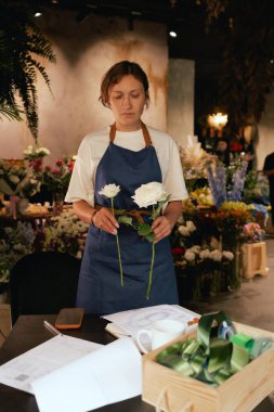 Önlüklü orta yaşlı kadın çiçekçi çiçekçide çiçek buketi için çiçek düzenliyor. Küçük bir yerel işletme. Dizinin bir parçası. Yumuşak odak