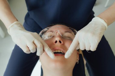 Genç bir dişçiye dişçi muayenesinde gülümseyen olgun bir kadın. Klinikte randevu. Diş beyazlatma, temizlik ya da oral, hastanede ağız ve sakız bakımı. Yumuşak odaklanma. Dizinin bir parçası. Yakın plan..