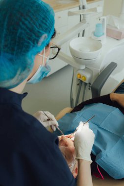 Genç bir dişçiye dişçi muayenesinde gülümseyen olgun bir kadın. Klinikte randevu. Diş beyazlatma, temizlik ya da oral, hastanede ağız ve sakız bakımı. Yumuşak odaklanma. Dizinin bir parçası. Yakın plan..