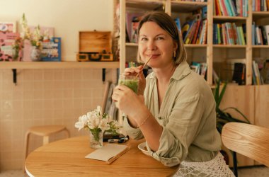 Orta yaşlı bir kadın sosyal medya yayınını rahat bir kafede cep telefonuna kaydırıyor. Küçük bir iş. İş için telefon kullanmak, online alışveriş, para transferi, finans, internet bankacılığı. Bir serinin parçası