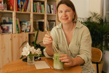 Orta yaşlı bir kadın sosyal medya yayınını rahat bir kafede cep telefonuna kaydırıyor. Küçük bir iş. İş için telefon kullanmak, online alışveriş, para transferi, finans, internet bankacılığı. Bir serinin parçası