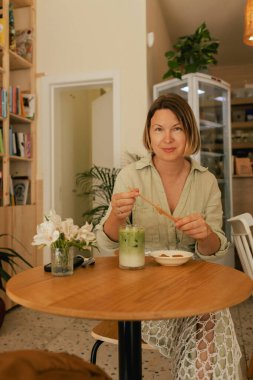 Orta yaşlı bir kadın sosyal medya yayınını rahat bir kafede cep telefonuna kaydırıyor. Küçük bir iş. İş için telefon kullanmak, online alışveriş, para transferi, finans, internet bankacılığı. Bir serinin parçası