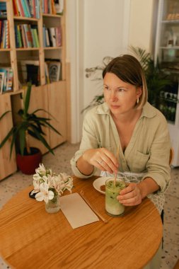 Orta yaşlı bir kadın sosyal medya yayınını rahat bir kafede cep telefonuna kaydırıyor. Küçük bir iş. İş için telefon kullanmak, online alışveriş, para transferi, finans, internet bankacılığı. Bir serinin parçası