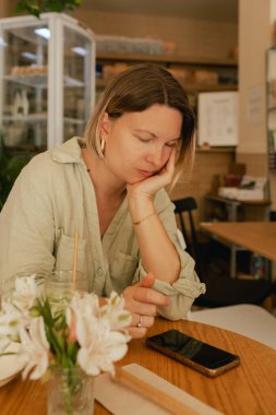 Orta yaşlı bir kadın sosyal medya yayınını rahat bir kafede cep telefonuna kaydırıyor. Küçük bir iş. İş için telefon kullanmak, online alışveriş, para transferi, finans, internet bankacılığı. Bir serinin parçası