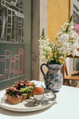 Etli sandviç, yumurta ve taze yeşillik. Güneşli açık kafede, ahşap masada sunulan lezzetli mahsul kahvaltısı. Bir serinin parçası.