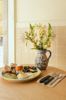 Etli sandviç, avokado, yumurta ve taze yeşillik. Güneşli kapalı kafeteryadaki ahşap masada servis edilen lezzetli mahsul kahvaltısı. Bir serinin parçası.