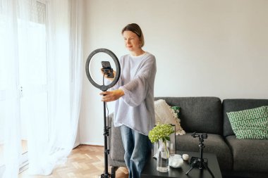 Orta yaşlı kadın güzellik blogcusu evde halka ışığıyla boks yaparken cilt bakımı yapıyor. Çevrimiçi mağaza tanıtımı için kullanıcı kaynaklı UGC içeriği. Vlogger canlı yayın yapıyor. Bir serinin parçası