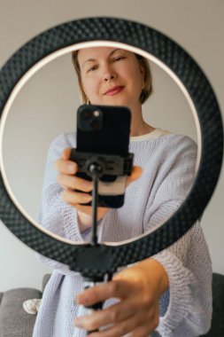 Orta yaşlı kadın güzellik blogcusu evde halka ışığıyla boks yaparken cilt bakımı yapıyor. Çevrimiçi mağaza tanıtımı için kullanıcı kaynaklı UGC içeriği. Vlogger canlı yayın yapıyor. Bir serinin parçası