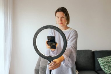 Orta yaşlı kadın güzellik blogcusu evde halka ışığıyla boks yaparken cilt bakımı yapıyor. Çevrimiçi mağaza tanıtımı için kullanıcı kaynaklı UGC içeriği. Vlogger canlı yayın yapıyor. Bir serinin parçası