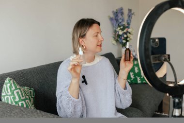 Orta yaşlı kadın güzellik blogcusu evde halka ışığıyla boks yaparken cilt bakımı yapıyor. Çevrimiçi mağaza tanıtımı için kullanıcı kaynaklı UGC içeriği. Vlogger canlı yayın yapıyor. Bir serinin parçası