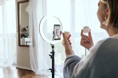 Orta yaşlı kadın güzellik blogcusu evde halka ışığıyla boks yaparken cilt bakımı yapıyor. Çevrimiçi mağaza tanıtımı için kullanıcı kaynaklı UGC içeriği. Vlogger canlı yayın yapıyor. Bir serinin parçası