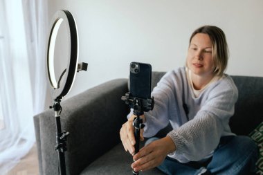 Orta yaşlı kadın güzellik blogcusu evde halka ışığıyla boks yaparken cilt bakımı yapıyor. Çevrimiçi mağaza tanıtımı için kullanıcı kaynaklı UGC içeriği. Vlogger canlı yayın yapıyor. Bir serinin parçası