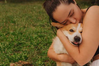Güneşli bir havada parkta Galli bir Corgi 'ye sarılan bir kadının yakın çekimi. Köpeği gezdirme kavramı, köpek ve sahibi arasındaki arkadaşlık. Dizinin bir parçası. Yumuşak odak.