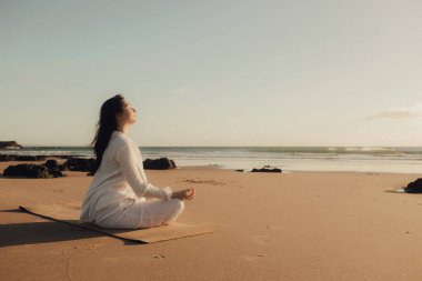 Beyaz elbiseli Asyalı kadın meditasyon için yoga yapıyor ve deniz kenarında sağlıklı olmak için dinleniyor. Sağlık hizmeti egzersizi ve yoga konsepti. Solo turizm. Bir serinin parçası.